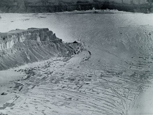 Jemen, 1932, Heinin, HET PORTAAL VAN EIGENLIJK HADRAMAUT UIT DE LUCHT GEZIEN. In heb midden de stervende stad Heinin, die verzwolgen wordt door de zandzee. Op den voorgrond een soort sawah-systeem; de hoogst enkele keeren dat heb regent wordt tusschen de dijkjes het water uit de dan overstroomende rivieren vastgehouden. Bij het bezoek van den schrijver aan Heinin had het daar sinds eenige jaren niet geregend.