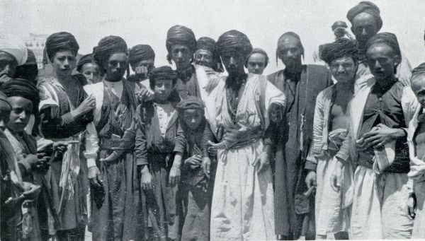 Jemen, 1933, Onbekend, WELGESTELDE KOOPLUI IN JEMEN. N JOOD ( ZONDER TULBAND) STAAT OP UITDRUKKELIJK VERZOEK VAN DEN SCHRIJVER IN HUN MIDDEN