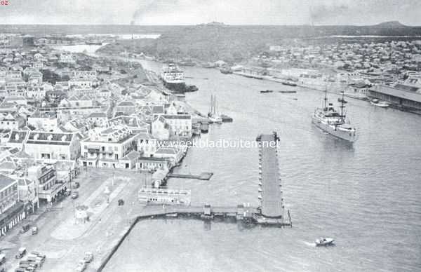 Curaao, 1934, Willemstad, Curaao voorheen en thans. Curaao, de haven van Willemstad. Op den voorgrond de geopende pontonbrug, de koningin Emmabrug, die de twee helften der stad verbindt. Rechts het Brionplein en een gedeelte van Otrabanda (de overzijde). Op den achtergrond in het midden fort Nassau