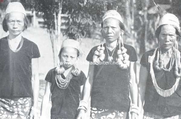 Het toilet der Apo-Kajans van Centraal Borneo. Vrouwen der Apo-Kajans in ouderwetsche kleeding, waarop drakenfiguren. Duidelijk zichtbaar zijn de lange oorlellen, die bij de vrouw links op de foto doorgescheurd zijn. Dit schoonheidsgebrek wordt gecamoufleerd, door met de haren de ooren te verbergen